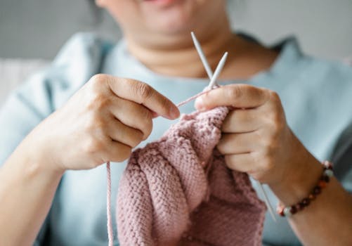 Crop mature female resting at home and knitting with pink yarn and needles